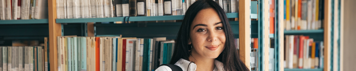 College student standing in front of bookcase in library