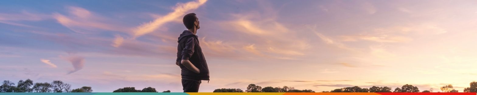a man standing in a field watching a sunset