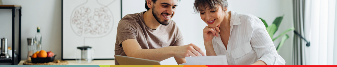 Happy couple sitting at laptop smiling after understanding how much to invest each to reach their goals